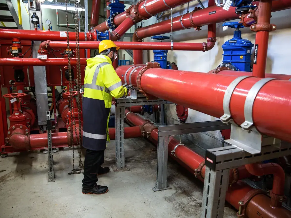 Technician in a hard hat and hi-vis jacket inspecting piping in a commercial mechanical room in Costa Mesa, CA
