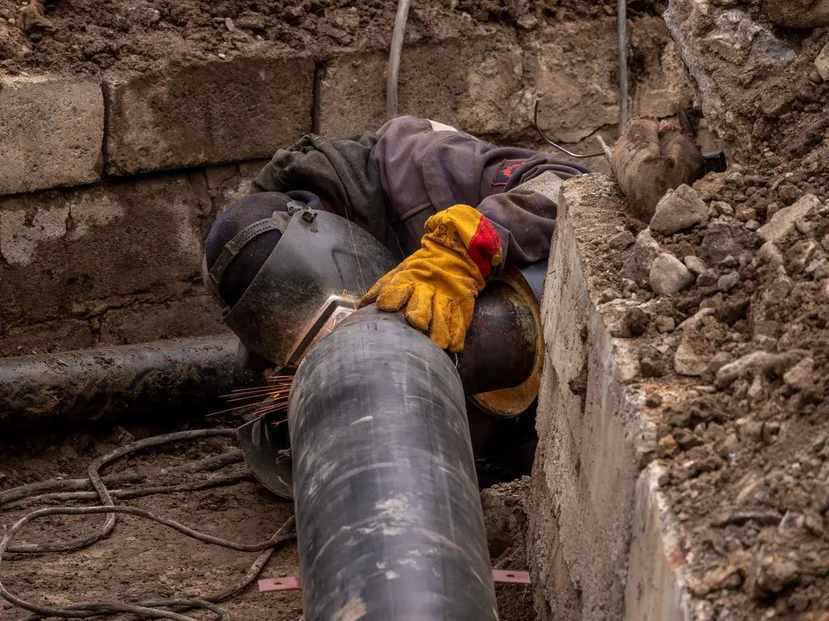 Worker in a welding helmet joining steel pipe inside a narrow excavation, the kind of targeted dig planned from camera findings in Newport Beach, CA