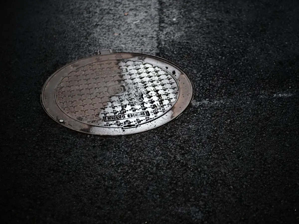 Steel sewer manhole cover set in dark asphalt on a street in Orange, CA