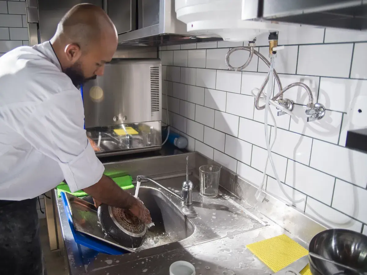 Chef rinsing cookware at a stainless commercial dish sink, a daily source of grease in Fullerton, CA kitchen drain lines Chef rinsing cookware at a stainless commercial dish sink, a daily source of grease in Fullerton, CA kitchen drain lines