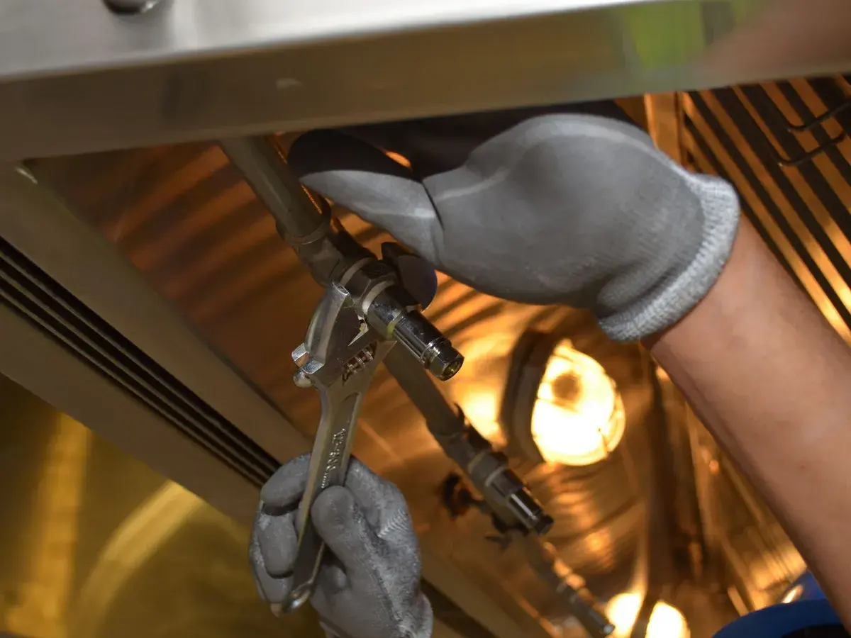 Gloved hands turning an adjustable wrench on overhead pipe in a commercial building ceiling in Anaheim, CA Gloved hands turning an adjustable wrench on overhead pipe in a commercial building ceiling in Anaheim, CA