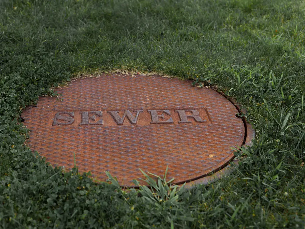 Rusted cast iron manhole cover marked SEWER set in a grass lawn in Fountain Valley, CA Rusted cast iron manhole cover marked SEWER set in a grass lawn in Fountain Valley, CA