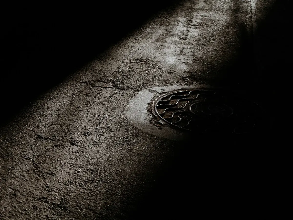 Sewer manhole cover lit by a single streetlight on a dark street in Garden Grove, CA Sewer manhole cover lit by a single streetlight on a dark street in Garden Grove, CA
